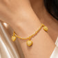 A close-up of a gold chain bracelet with three heart-shaped charms, worn on a person's wrist. The heart charms are detailed with small clear stones.