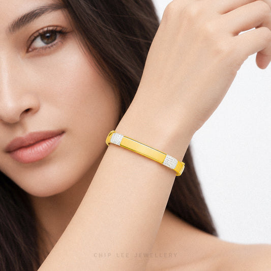 A close-up lifestyle shot of a model wearing a yellow gold bangle bracelet with pavé-set clear stones on the ends. The brand name 'CHIP LEE JEWELLERY' is subtly watermarked at the bottom.