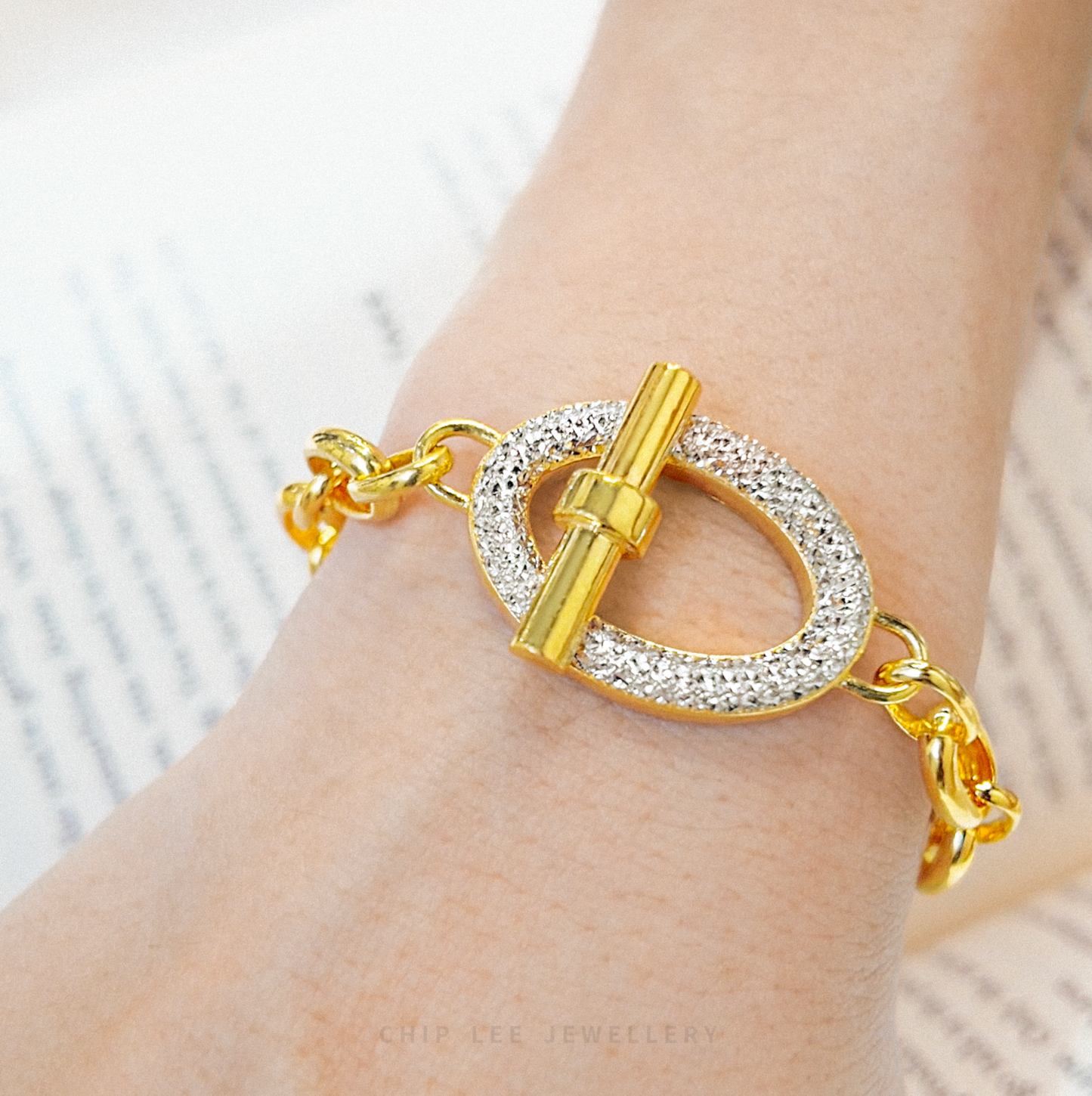 Gold bracelet with a clasp on a wrist against a neutral background
