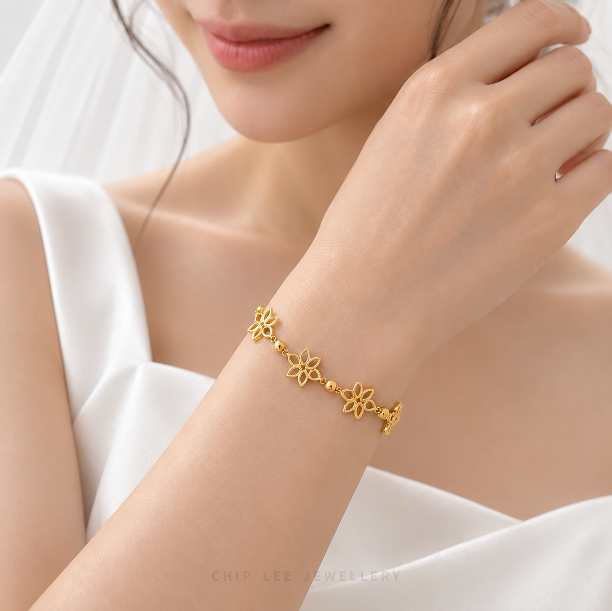 A close-up lifestyle shot of a model wearing a delicate gold bracelet with three flower motifs and a toggle clasp, styled with a white dress and veil.