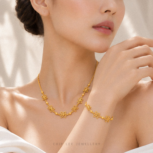 A close-up lifestyle shot of a model wearing a delicate gold necklace and matching bracelet from Chip Lee Jewellery. The jewelry features small, repeating floral/starburst motifs connected by tiny gold beads.