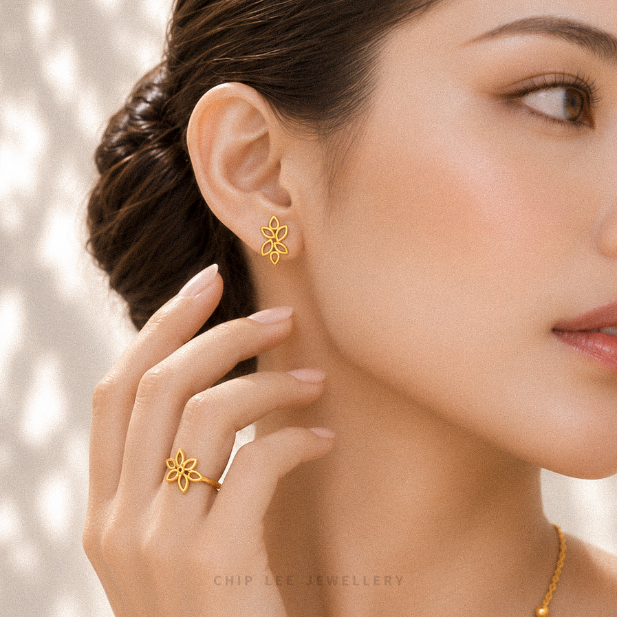 A close-up lifestyle shot of a woman wearing a delicate gold flower-shaped stud earring and matching ring, with her hand gently touching her neck. The brand name 'CHIP LEE JEWELLERY' is subtly printed at the bottom.