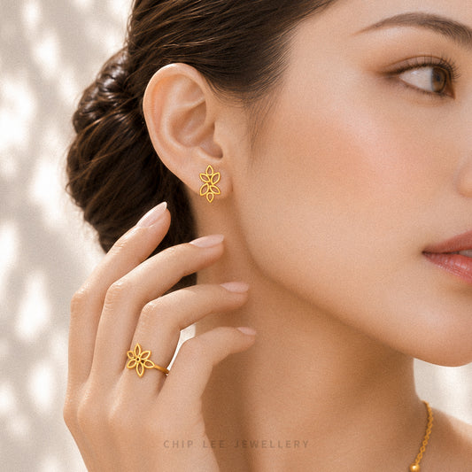 A close-up lifestyle shot of a woman wearing a delicate gold flower-shaped stud earring and matching ring, with her hand gently touching her neck. The brand name 'CHIP LEE JEWELLERY' is subtly printed at the bottom.