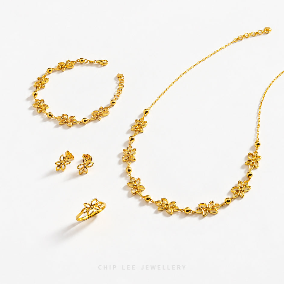 Gold jewelry set by Chip Lee Jewellery featuring a necklace, bracelet, earrings, and ring, all decorated with small flower motifs and polished bead details, arranged on a clean white background.