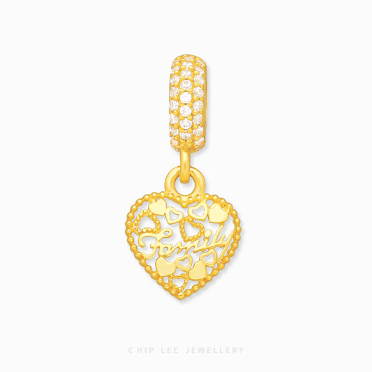 A gold charm in the shape of a heart with a family design, featuring intricate cut-out patterns and a small diamond-like embellishment at the top.