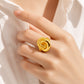 A close-up of a hand wearing a chunky, polished gold ring with a textured knot-like design, styled with a white collared shirt.