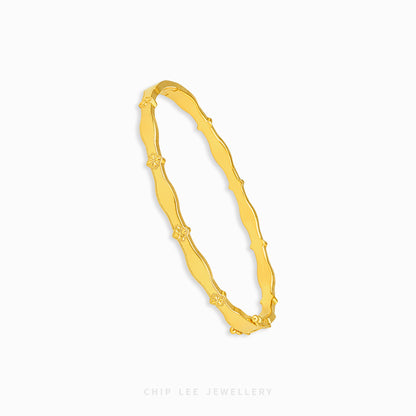 A gold bangle bracelet with a wavy, textured design and small floral details spaced along the band, shown on a plain white background with the brand name 'CHIP LEE JEWELLERY' printed at the bottom.