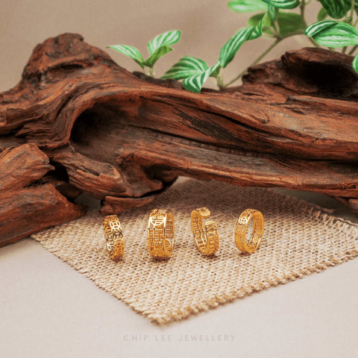 Four 916 gold rings with intricate symbolic engravings displayed on woven fabric beneath natural wood decor.