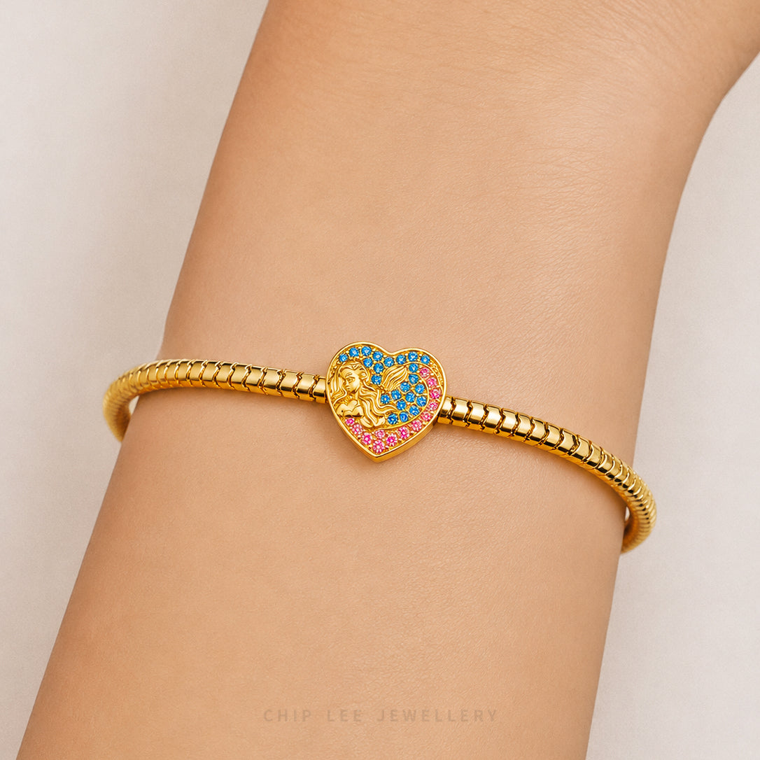 A gold-plated snake-braided bracelet with a heart-shaped charm featuring a lion and colorful enamel details, shown worn on a person's wrist.