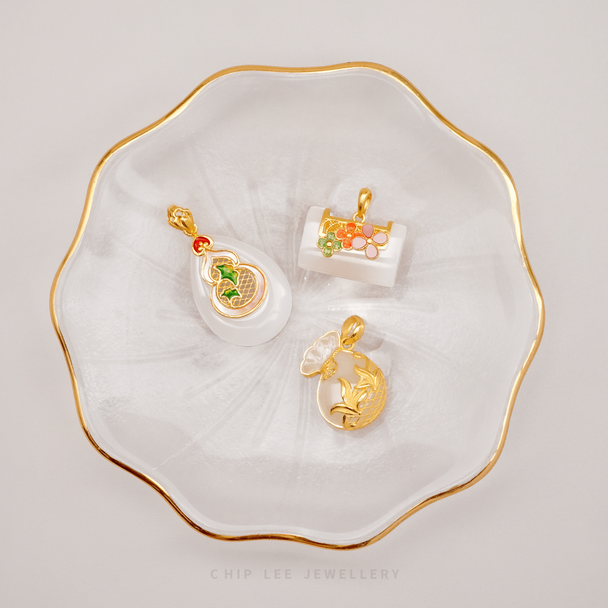 Gold and colorful pendants on a white dish with gold rim, featuring 'Chip Lee Jewellery'.