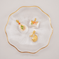 Gold and colorful pendants on a white dish with gold rim, featuring 'Chip Lee Jewellery'.