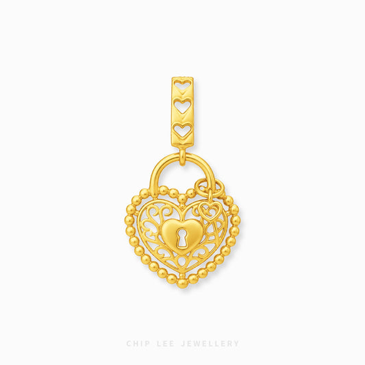 A gold heart-shaped charm with an intricate filigree design, a keyhole motif in the center, and a beaded border, shown on a light gray background with a brand watermark at the bottom.