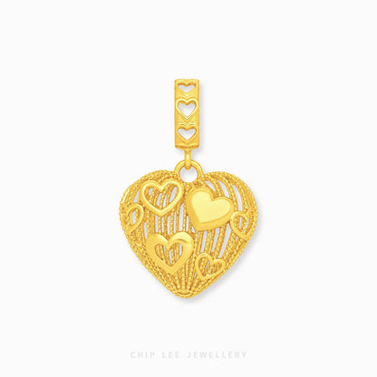 A gold heart-shaped charm with intricate cutout heart details and a textured border, shown on a clean white background with a brand watermark at the bottom.