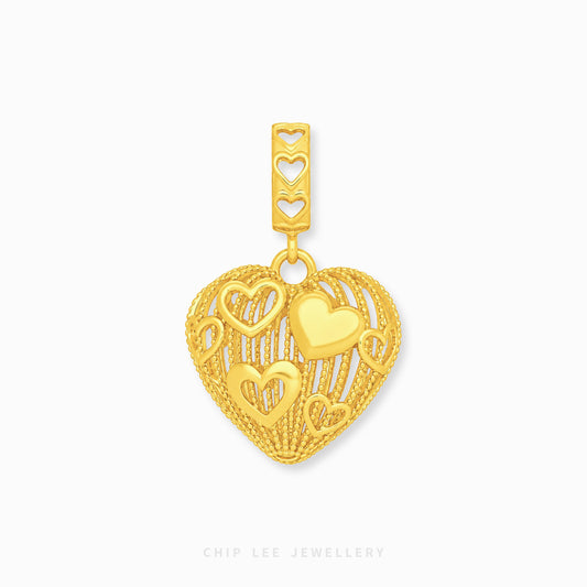A gold heart-shaped charm with intricate cutout heart details and a textured border, shown on a clean white background with a brand watermark at the bottom.