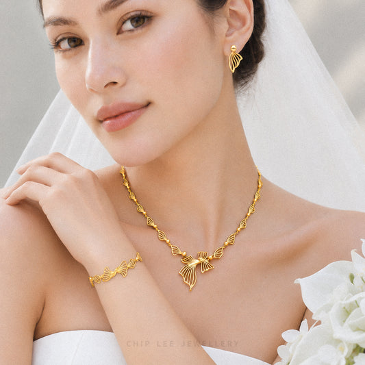 A close-up of a bride wearing a gold jewelry set from Chip Lee Jewellery, featuring a matching necklace, bracelet, and earring with a fan-like leaf design, set against a soft white bridal veil and bouquet.