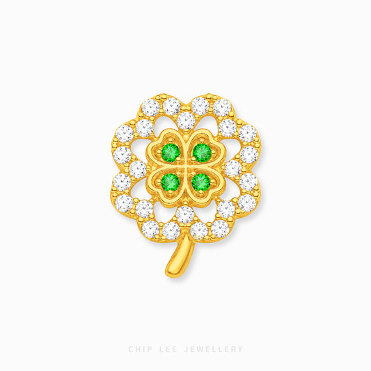 A gold four-leaf clover charm with four green gemstones in the center and a border of clear cubic zirconia stones, shown on a light gray background with a Chip Lee Jewellery watermark.