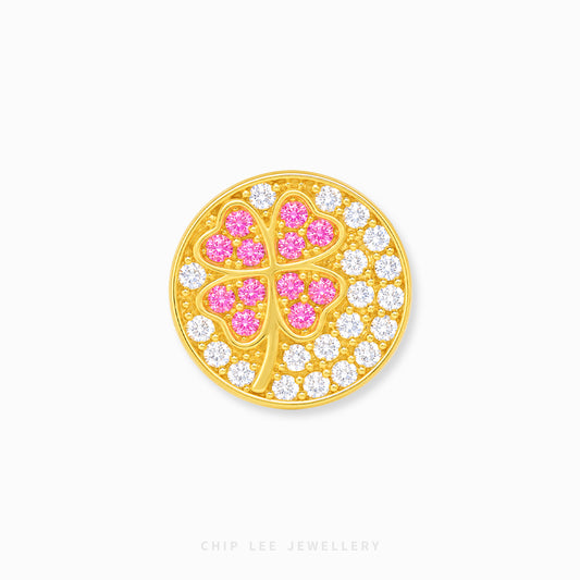 A round gold charm featuring a four-leaf clover design, with the center leaves set in pink stones and the surrounding border set in clear cubic zirconia, shown on a light gray background.