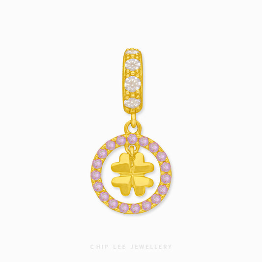 A gold charm featuring a clover design with a circle outline, studded with purple stones on the outline and a single clover inside.
