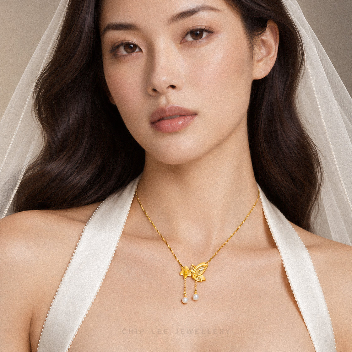 A close-up of a woman wearing a delicate gold necklace with a butterfly pendant and small pearl drops. She is wearing a white satin halter top and a sheer white veil, with the brand name 'CHIP LEE JEWELLERY' printed at the bottom.