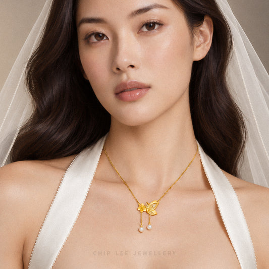 A close-up of a woman wearing a delicate gold necklace with a butterfly pendant and small pearl drops. She is wearing a white satin halter top and a sheer white veil, with the brand name 'CHIP LEE JEWELLERY' printed at the bottom.