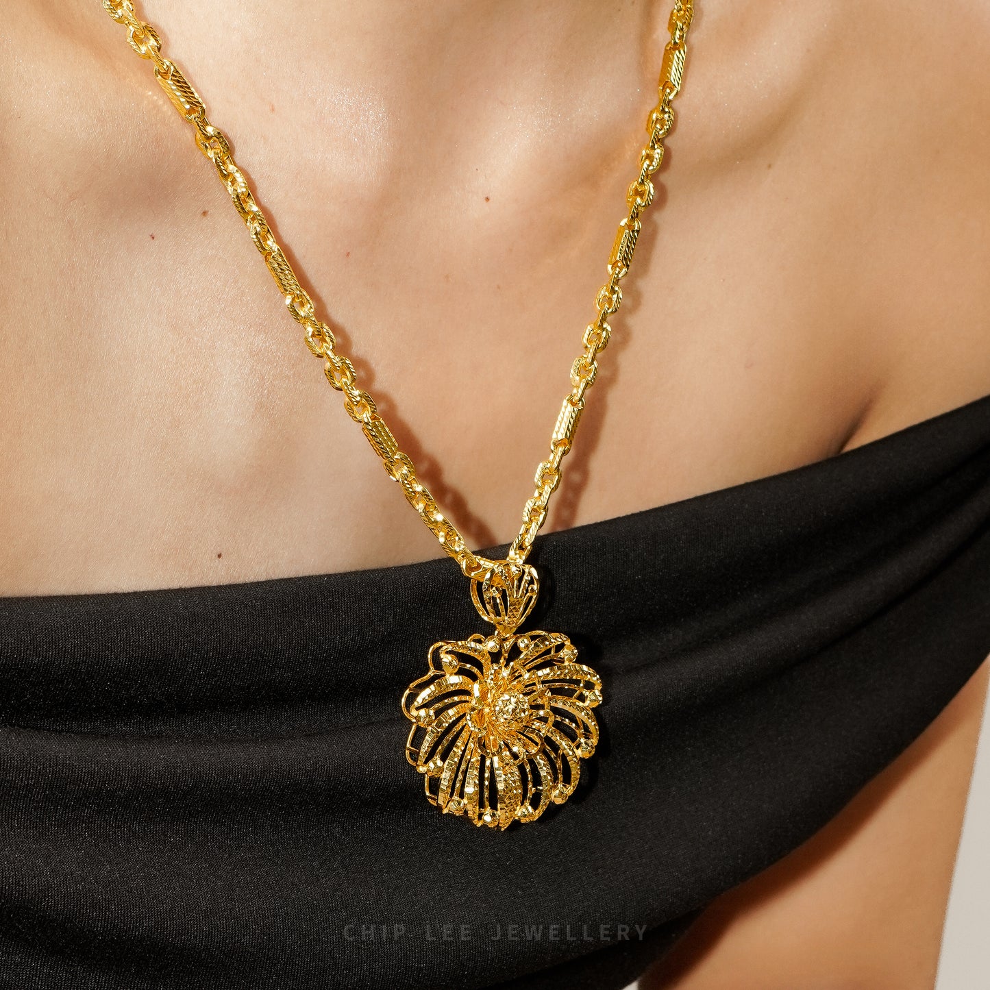 Close-up of a model wearing a gold chain with an intricate floral pendant against a black off-shoulder top.