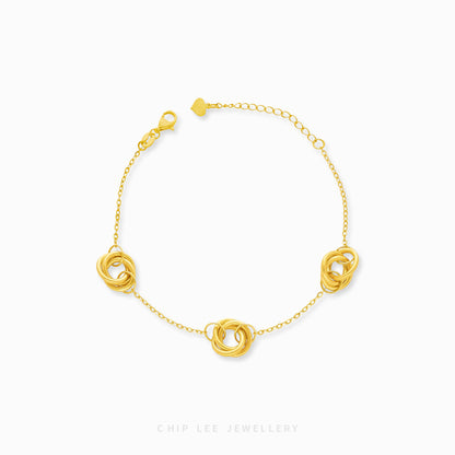 A gold bracelet featuring a series of trinity loop designs on a chain-link band with a clasp.