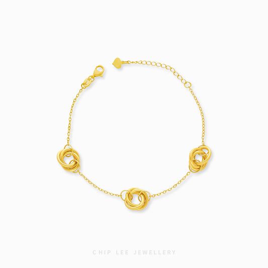 A gold bracelet featuring a series of trinity loop designs on a chain-link band with a clasp.