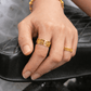 Close-up of a hand resting on a black chair, wearing 916 gold rings with intricate geometric and symbolic engravings.