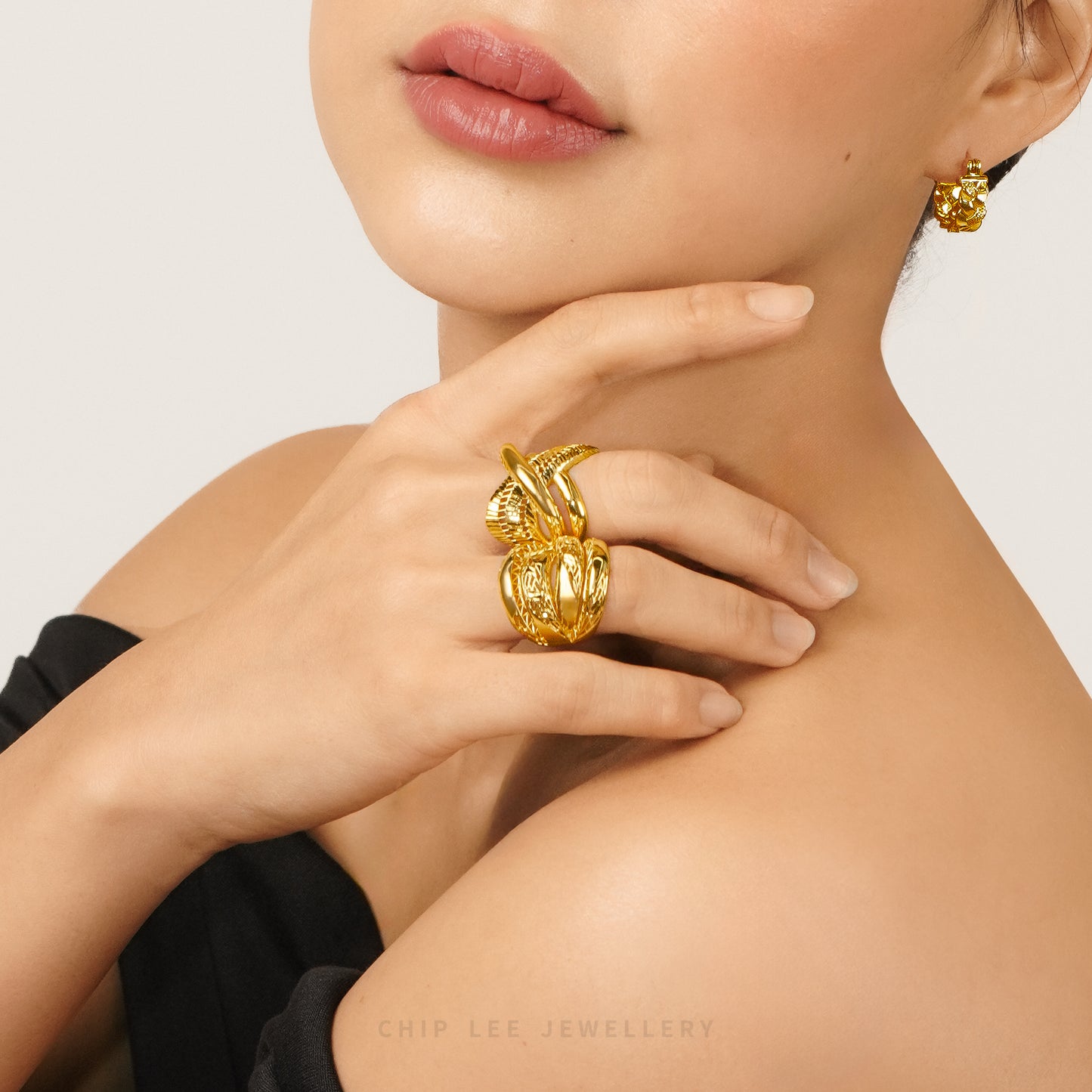 A close-up lifestyle shot of a model wearing a chunky, textured gold ring on her finger and a matching gold stud earring. The brand name 'CHIP LEE JEWELLERY' is watermarked at the bottom.