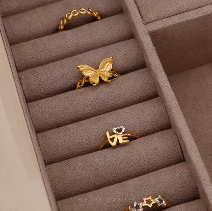 Gold butterfly and heart-shaped ring in a jewelry box with other rings.