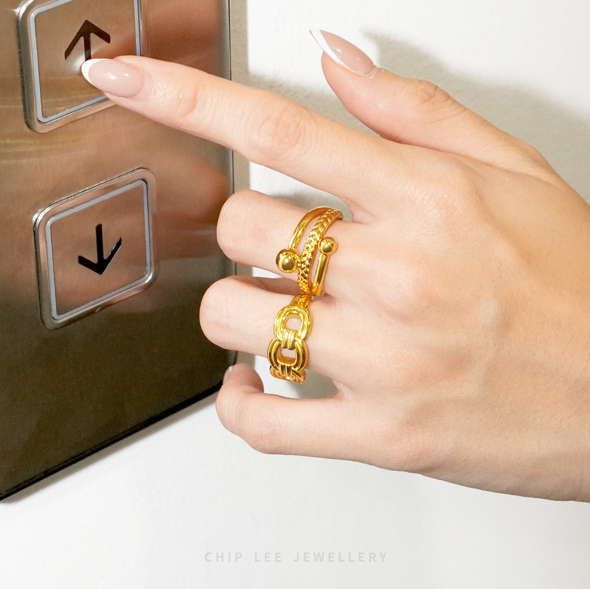 Hand pressing an elevator button with a gold ring on a neutral background