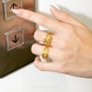 Hand pressing an elevator button with a gold ring on a neutral background