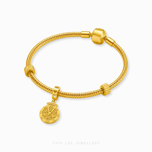 A gold-plated braided charm bracelet with a circular coin-style charm displayed on a clean white background with a brand watermark at the bottom.