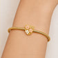 A gold snake-braided bracelet with a central shield-shaped charm featuring pink and white enamel flowers, shown worn on a person's wrist.