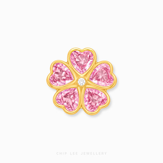 A gold flower-shaped charm featuring five pink heart-shaped gemstones and a small clear center stone, shown on a light gray background with Chip Lee Jewellery branding at the bottom.