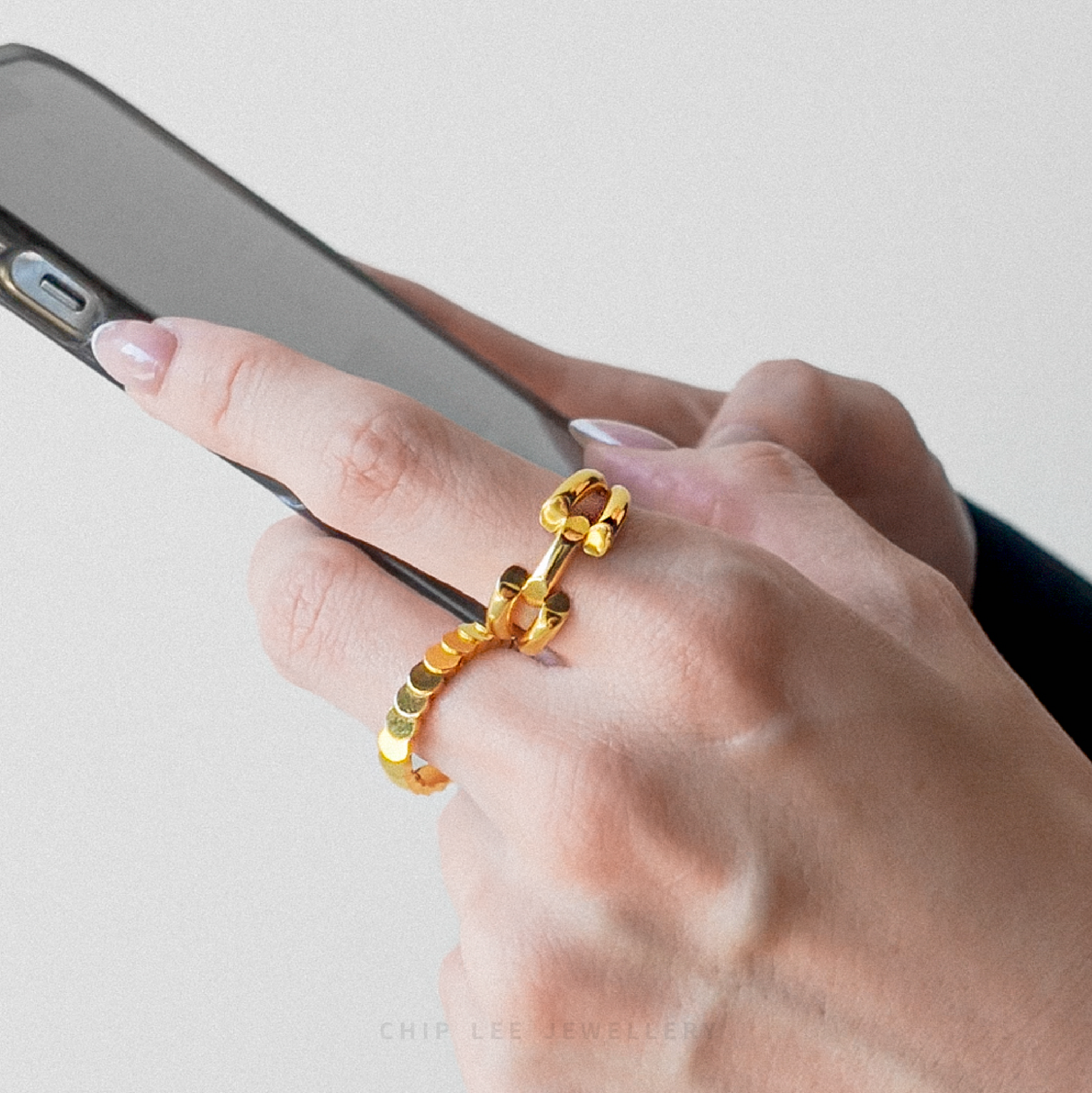 Hand wearing a gold ring holding a phone on a light background