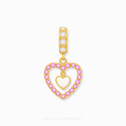 Gold heart-shaped dangle charm with a pink rhinestone border and a central gold heart, shown on a light gray background. The bail features three clear stones.