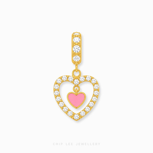 Gold heart-shaped pendant charm with a pink heart center, surrounded by clear pavé stones, on a light gray background.