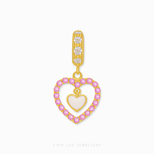 A gold charm in the shape of a heart with a smaller pink heart inside, encircled by small round diamonds.