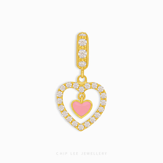 A gold charm in the shape of a heart with a smaller pink heart inside, encircled by small round diamonds.