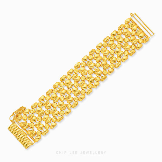 A gold multi-strand bracelet with textured and polished heart-shaped links, displayed diagonally on a clean white background with a brand watermark at the bottom.