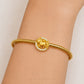 A gold-plated bangle bracelet with a central circular charm featuring a unicorn motif surrounded by small clear stones, shown worn on a person's wrist.