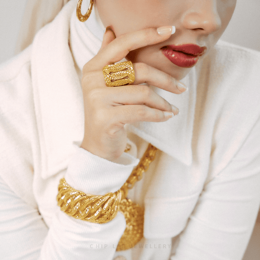 Close-up of a person wearing gold jewelry including earrings, ring, and bangle on a white background.