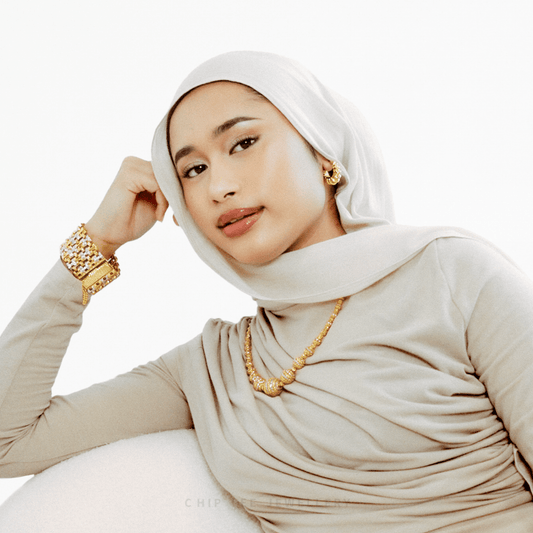 Woman wearing a beige hijab and gold jewelry on a white background
