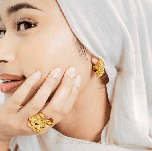 Woman wearing gold earrings and ring, with a soft focus on the jewellery.