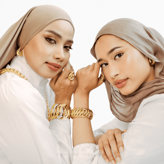 Two women wearing hijabs and gold jewelry on a white background