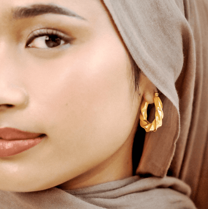 Close-up of a woman wearing gold hoop earrings with a neutral background