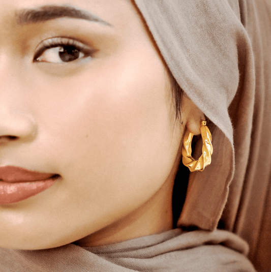 Close-up of a woman wearing gold hoop earrings with a neutral background