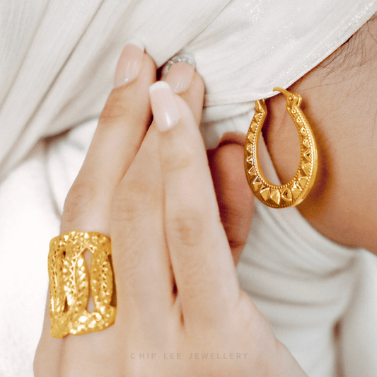 Gold hoop earrings and ring on a person's hand with a white background