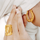 Gold hoop earrings and ring on a person's hand with a white background